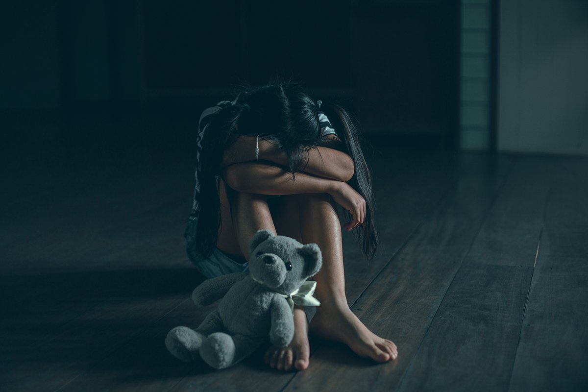 Sad little child girl sitting alone with teddy bear on floor