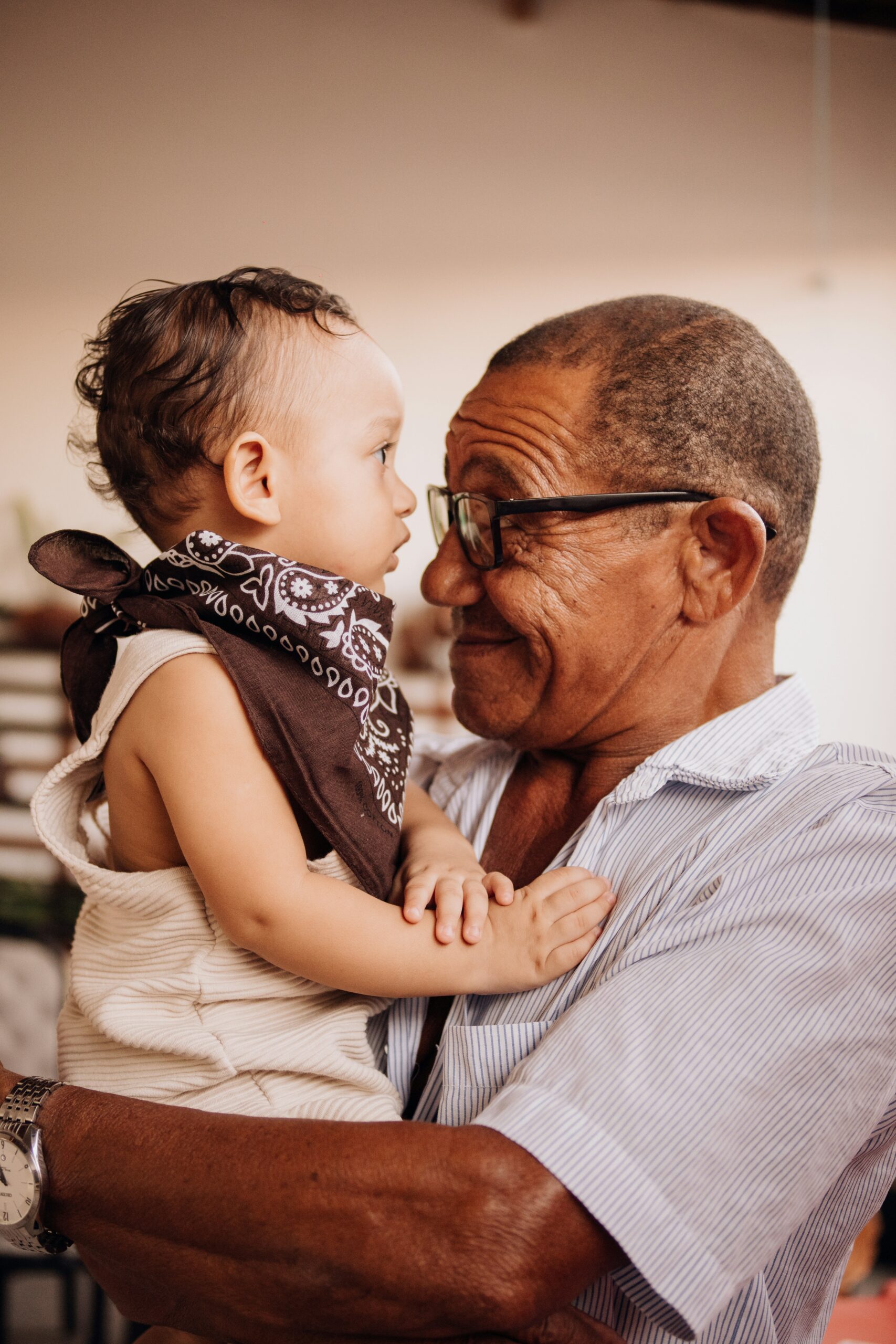 jeferson-santu-vh8T3QwFPkk-unsplash decorative image: an older gentleman with glasses holding a young child up to his face